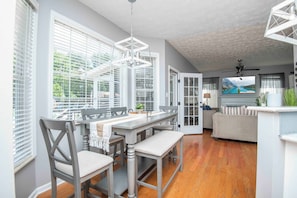 A dining area with a table, chairs, and a bench. There is a sofa and a television in the background. - Knoxville Escape - Resort Style Backyard - Pool, Hot Tub, Sauna - Sleeps 15 (Knoxville)