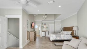 A bedroom with a bed, a nightstand, a lamp, a dresser, a TV, and a chandelier. - Beach Pointe 203 (Destin)
