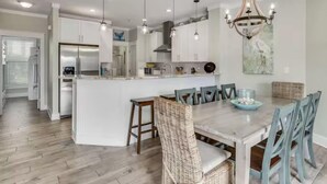 A modern kitchen with white cabinets, a central island, and a dining area with wicker chairs. - Beach Pointe 203 (Destin)
