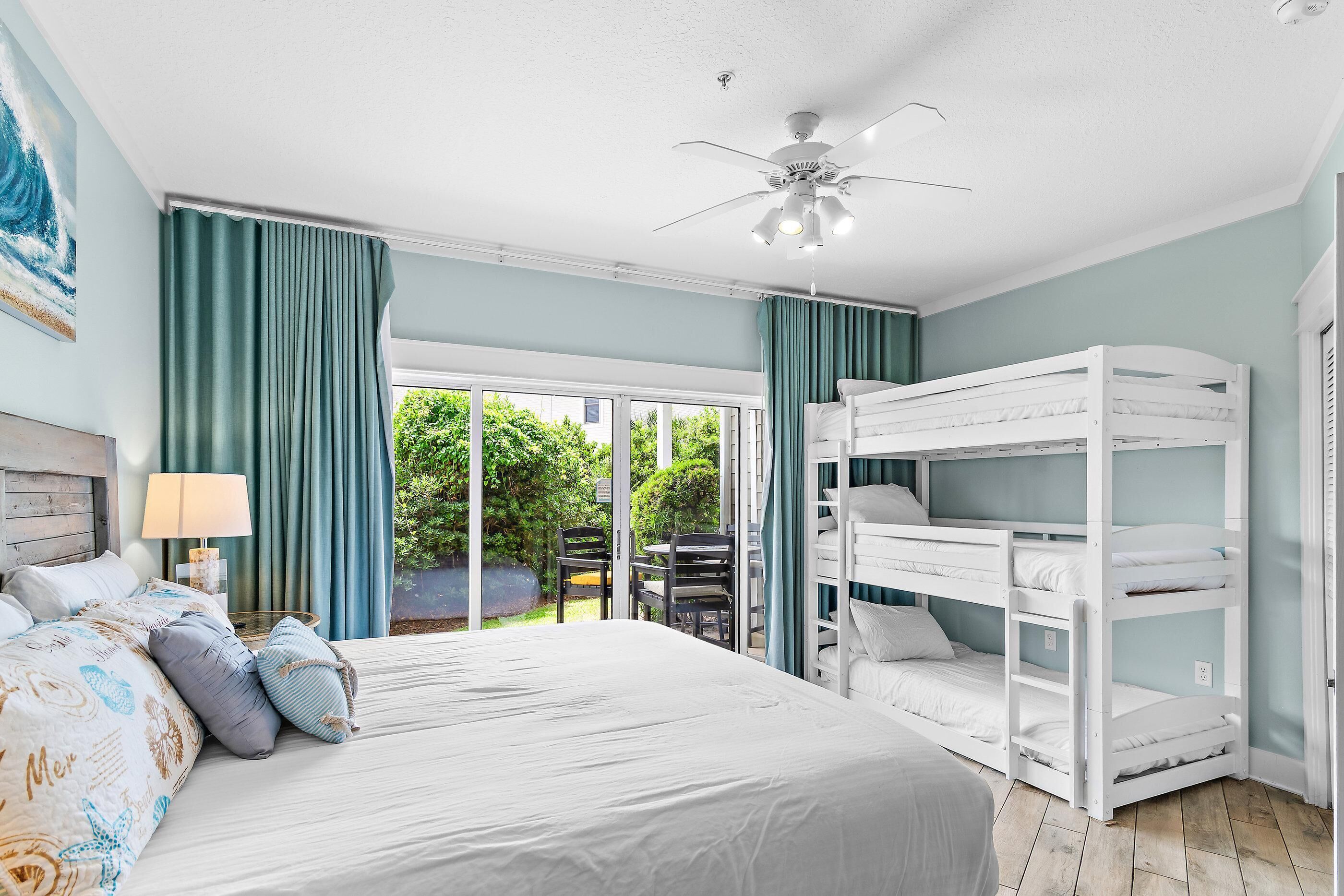 A bedroom with a bed, bunk beds, a ceiling fan, and a view of greenery outside.