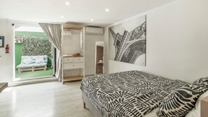 A bedroom with a bed, a dresser, a mirror, and a door leading to a balcony with a green wall and a bench. - Vacation Home 'Ita' with Private Terrace, Wi-Fi and Air Conditioning (Mogán)