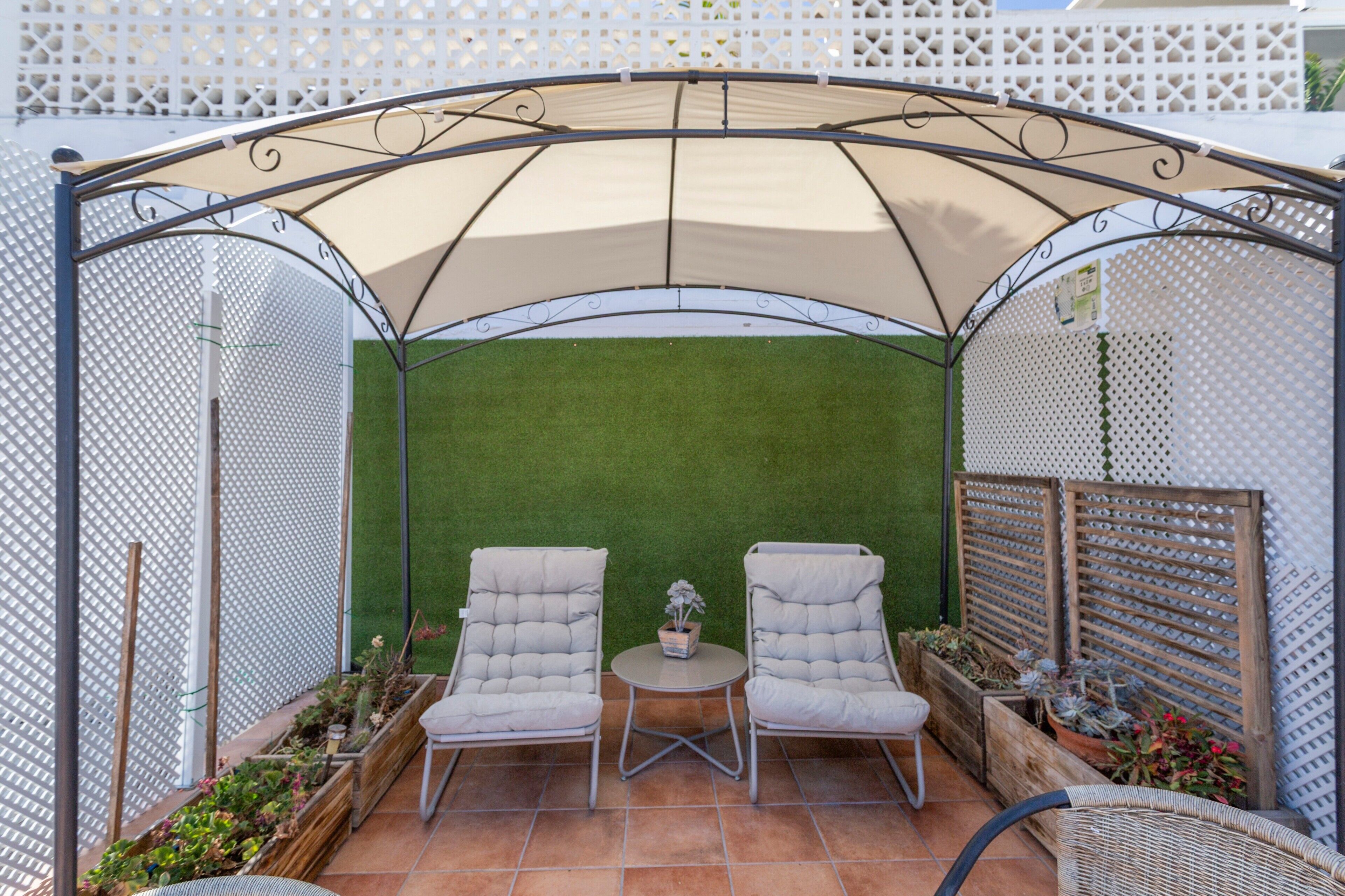 Een overdekt terras met twee comfortabele stoelen, een kleine tafel en een potplant.
