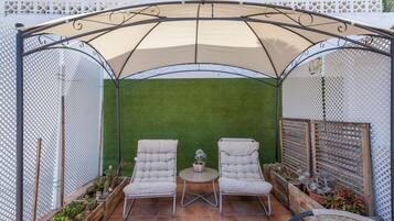 Een overdekt terras met twee comfortabele stoelen, een kleine tafel en een potplant.
