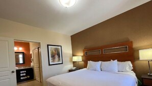 Een hotelkamer met een bed, nachtlampjes, een nachtkastje, een bureau, een stoel, een spiegel en een deur naar een badkamer.