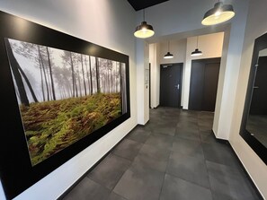 A hallway with a large framed forest photograph, pendant lighting, and a door at the end. - Anglet Cinq Cantons - T2 with balcony (Anglet)