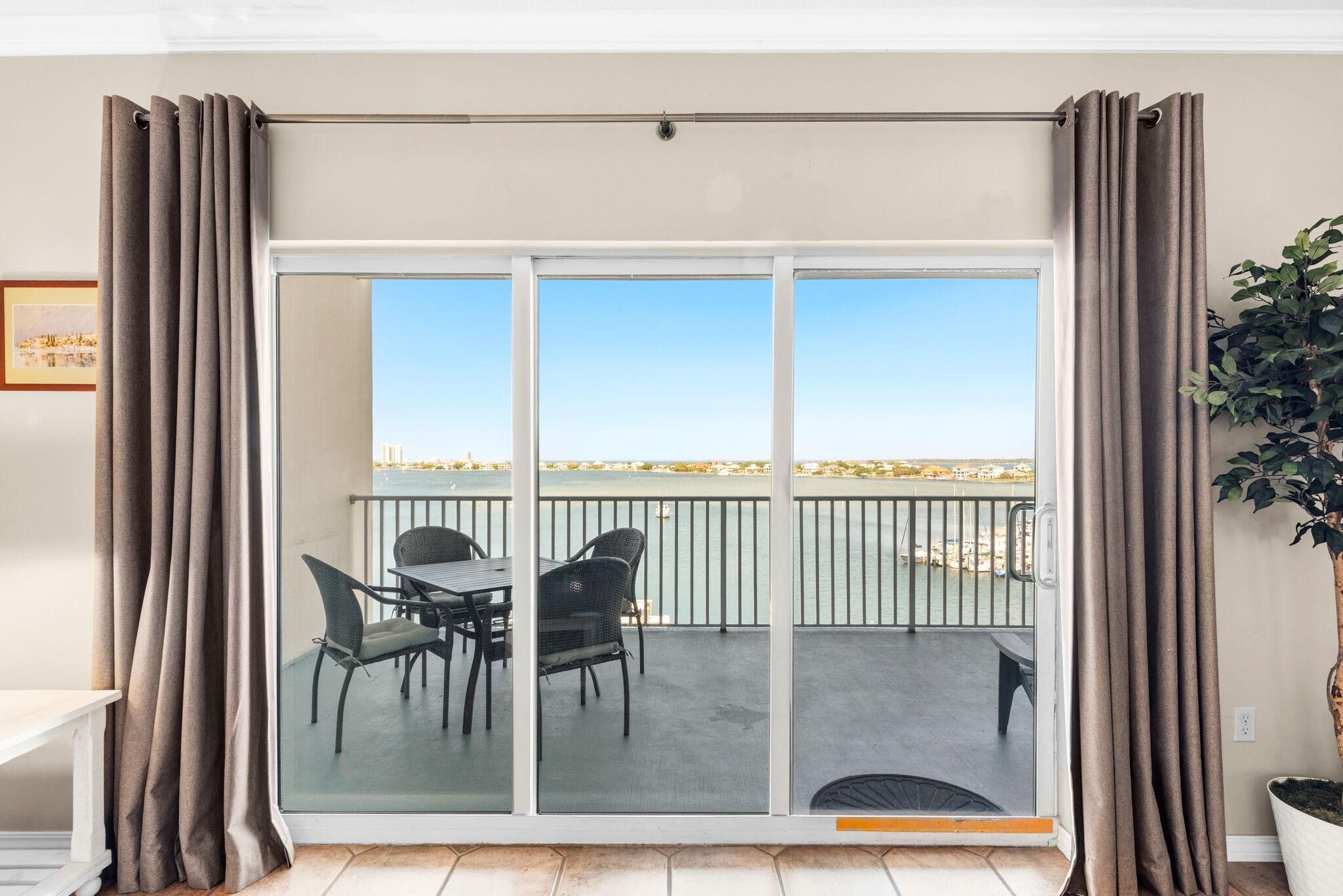 Un balcone con tavolo e sedie, vista sul mare e una pianta a destra.