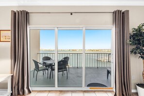 A balcony with a table and chairs, a view of the sea, and a plant on the right.