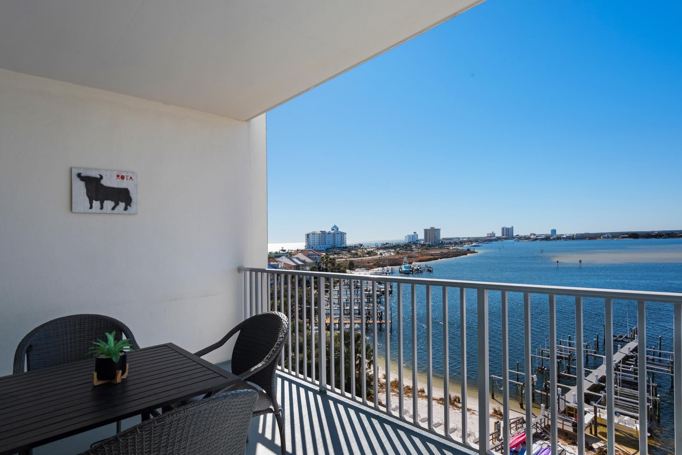A balcony with a view of a waterfront, a table with chairs, and a bull silhouette decoration.