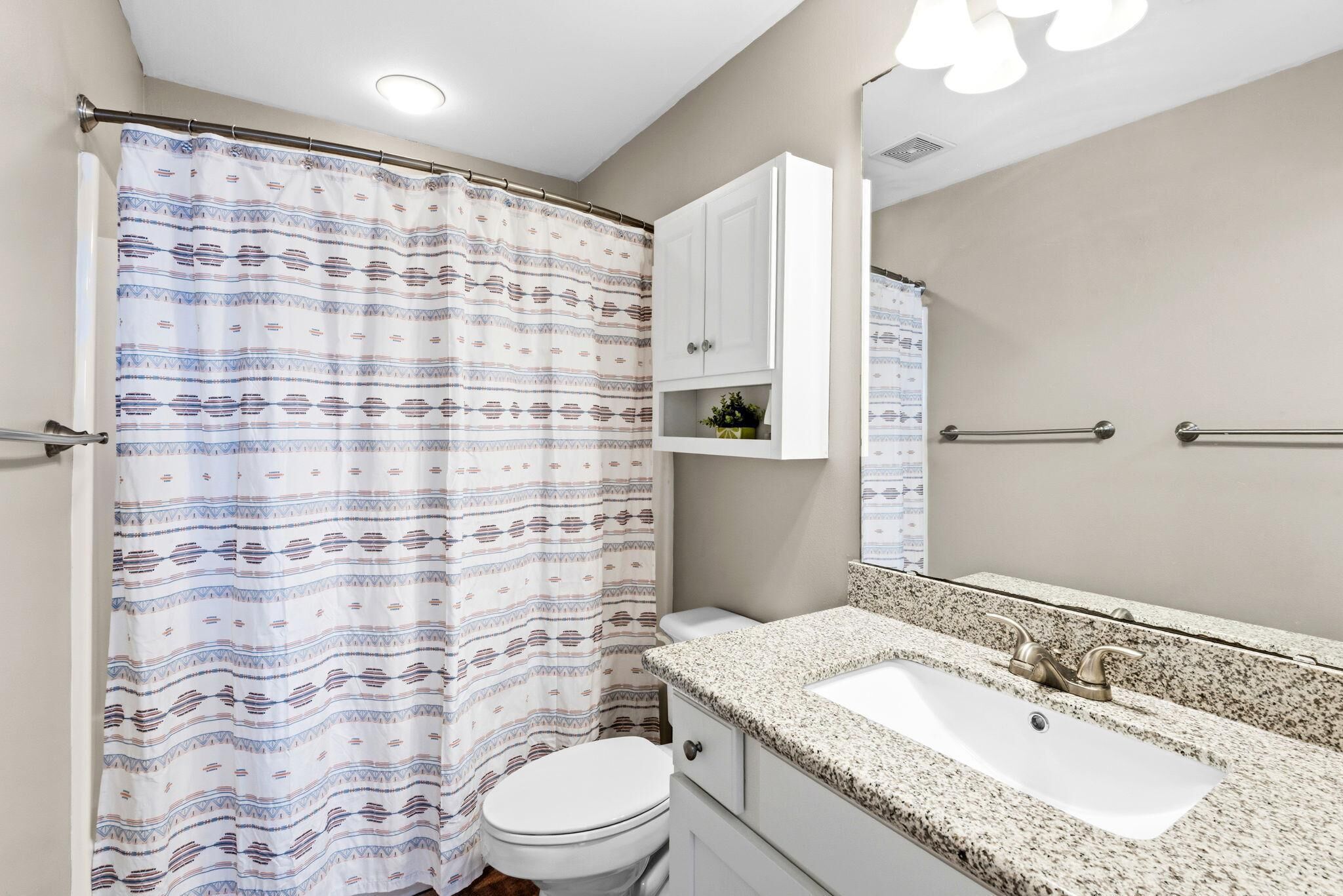 A bathroom with a shower curtain, toilet, sink, and cabinet.