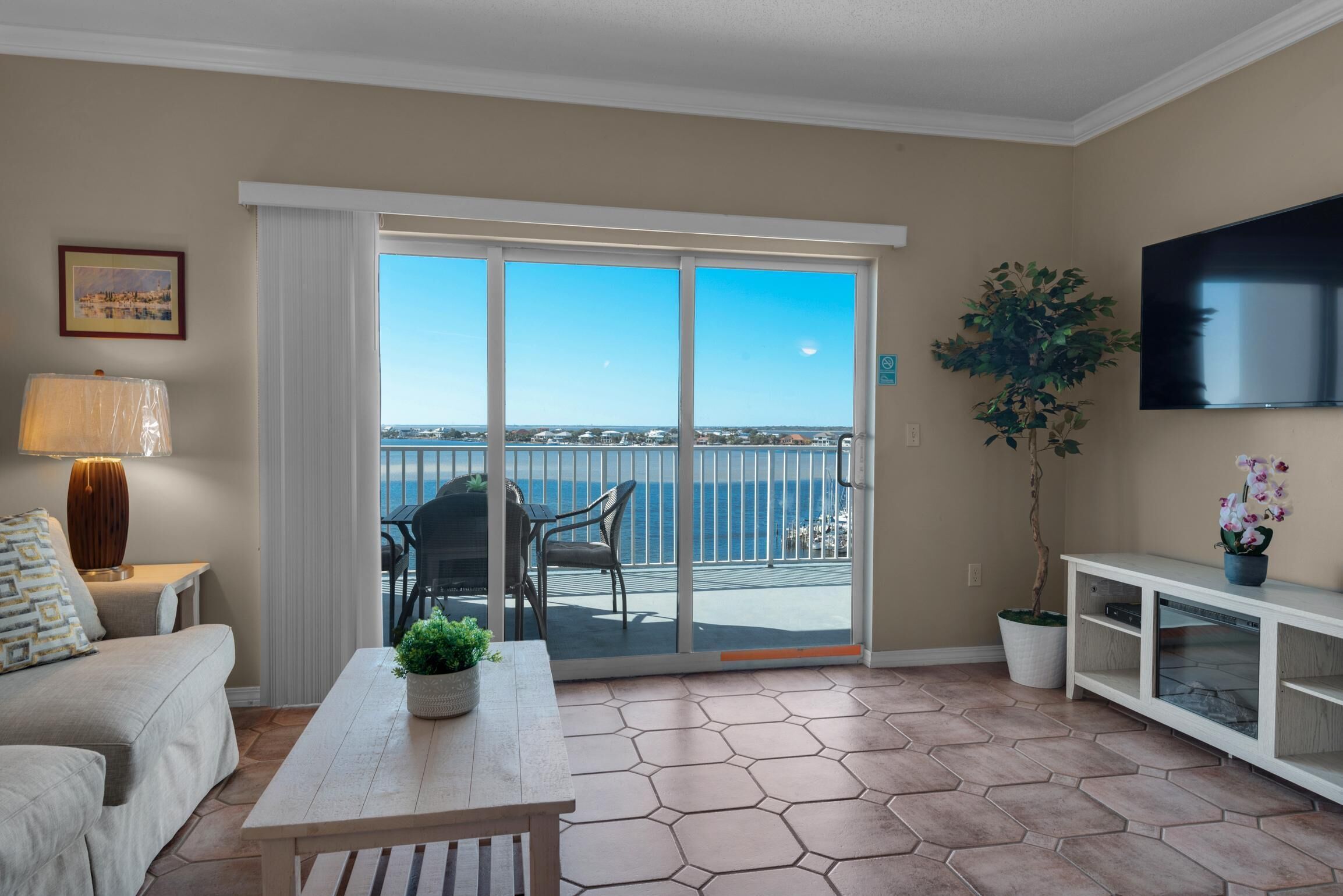 A living room with a sofa, a coffee table, a TV, a plant, and a balcony with a view of the sea.