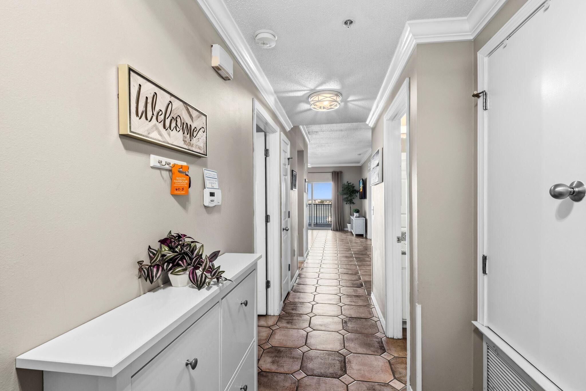 A hallway with a welcome sign, a thermostat, and a potted plant.