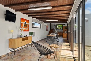 A modern interior with a wooden ceiling, a TV mounted on the wall, a dining area with chairs and a table, and a kitchen visible through glass doors. - Vacation Apartment 'Guada' with Private Terrace, Wi-Fi and Air Conditioning (Tao)