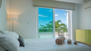 Une chambre à coucher avec un lit, une lampe, un balcon donnant sur un paysage verdoyant et une armoire jaune.