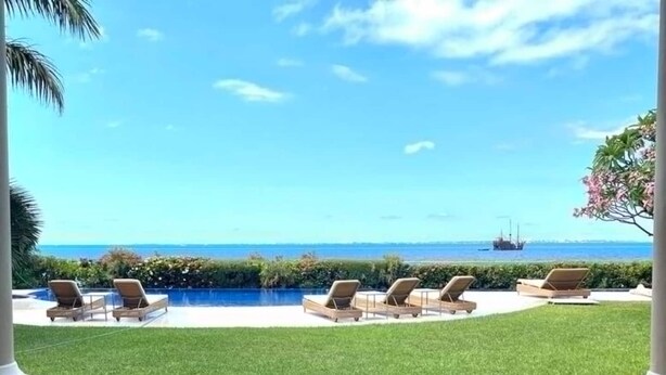 Un espace piscine doté de chaises longues, d’une pelouse bien entretenue et offrant une vue dégagée sur l’océan.