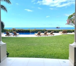A pool area with lounge chairs, a well-maintained lawn, and a clear view of the ocean. - Villa Bianca Beachfront Luxury Living w Gym Chef (Cancun)