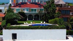 Un bâtiment moderne doté d’une piscine, entouré d’une plage de sable blanc et bordé d’une eau turquoise cristalline.