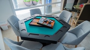 Une table de billard recouverte d’un drap vert, entourée de quatre chaises grises.