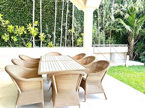 A patio with a white table and wicker chairs, surrounded by greenery. - Villa Bianca Beachfront Luxury Living w Gym Chef (Cancun)