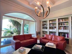 A spacious living room with two red leather sofas, a coffee table, and a large bookshelf filled with books. - Villa Bianca Beachfront Luxury Living w Gym Chef (Cancun)