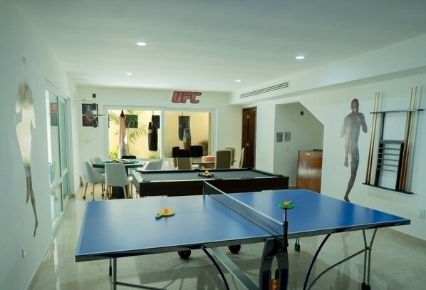 A room with a ping pong table, a seating area with chairs, and a UFC sign on the wall. - Villa Bianca Beachfront Luxury Living w Gym Chef (Cancun)
