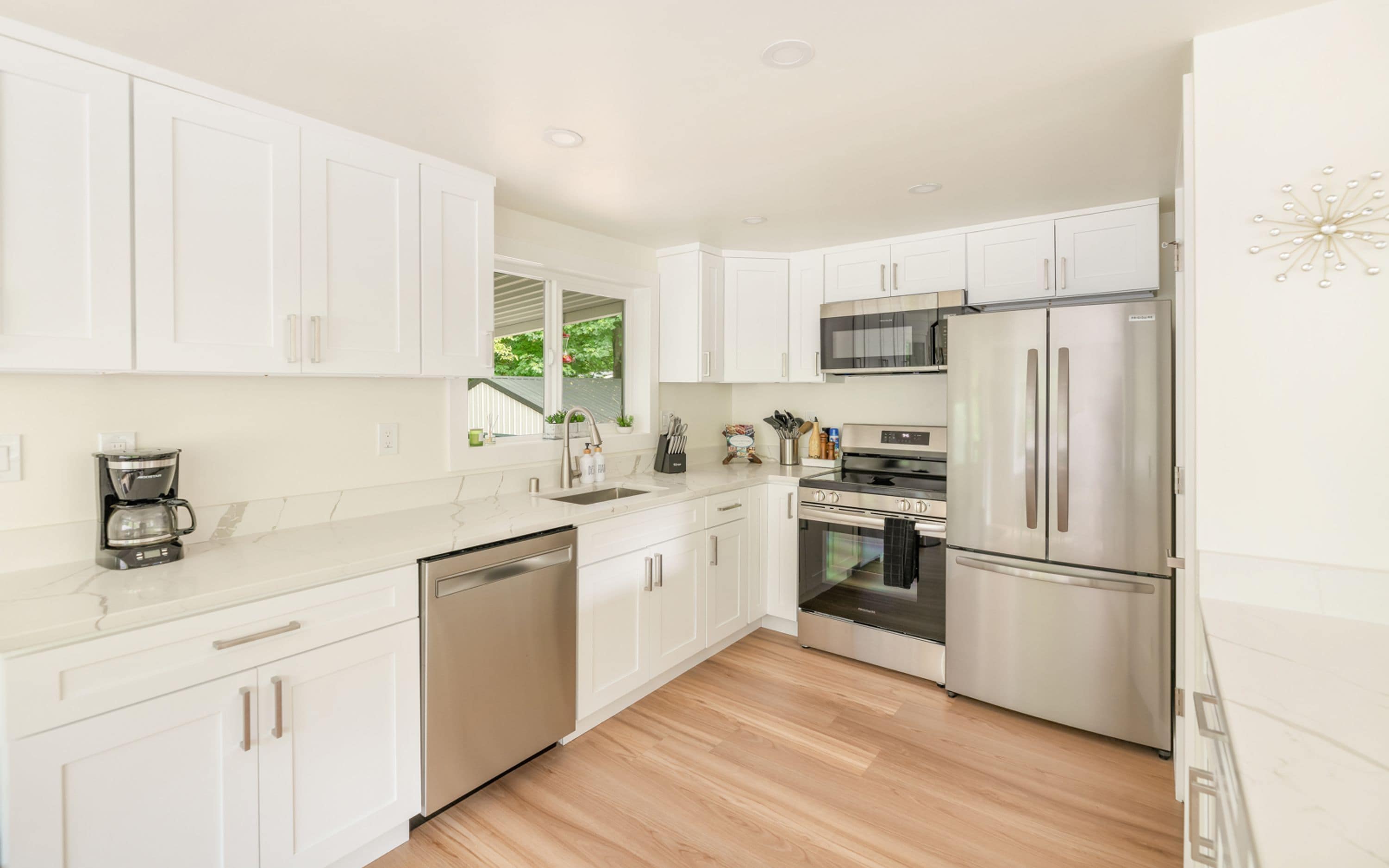 Una cocina moderna con armarios blancos, electrodomésticos de acero inoxidable y piso de madera.