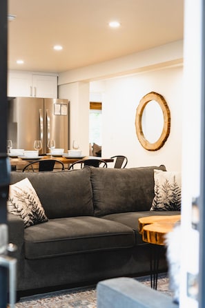 A modern living room with a grey sofa, a wooden coffee table, and a dining area with a white table and chairs.