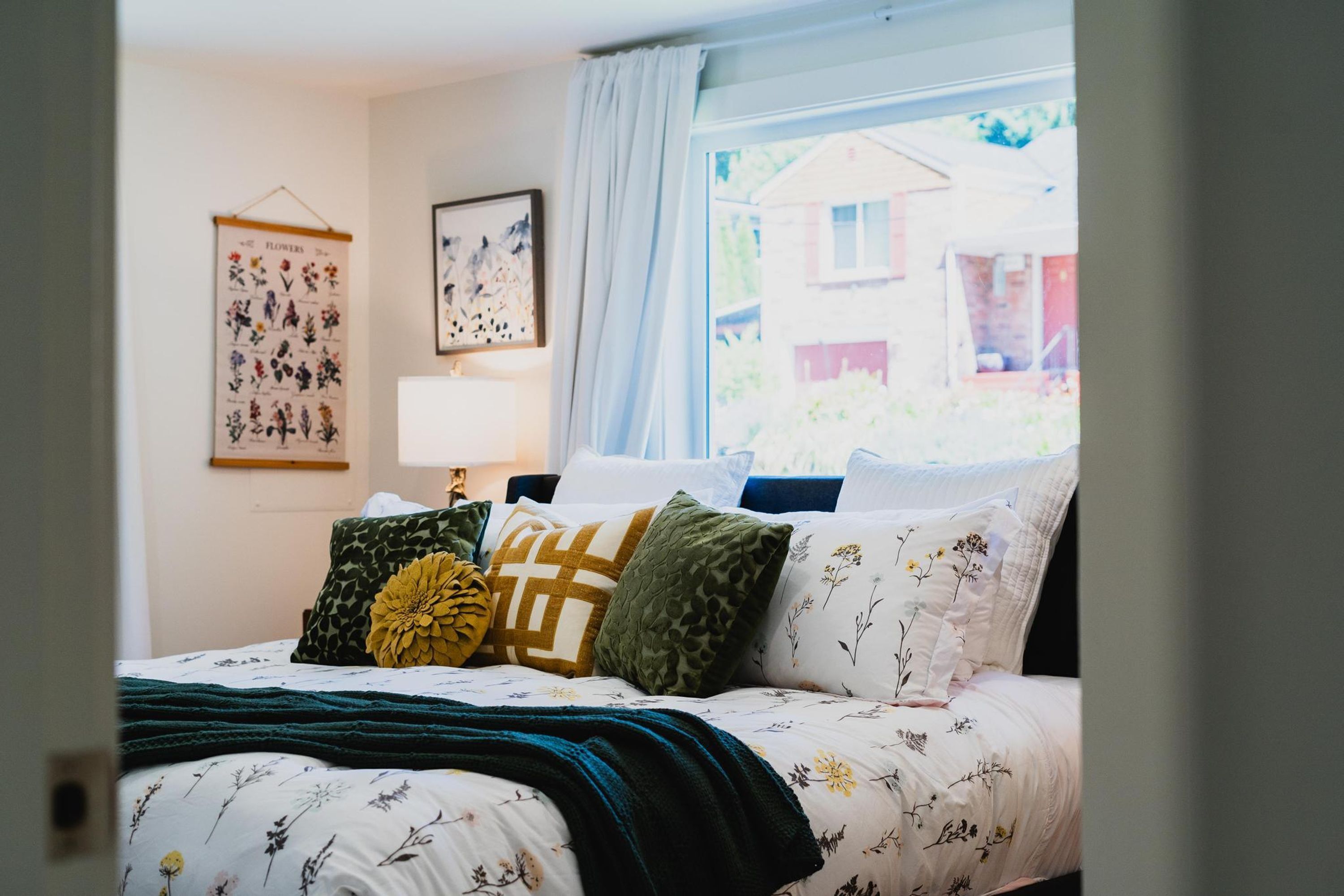 Une chambre à coucher avec un lit, des oreillers, une fenêtre et un mur orné d’un motif floral.