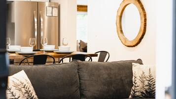 A modern living room with a grey sofa, a wooden coffee table, and a dining area with a white table and chairs.