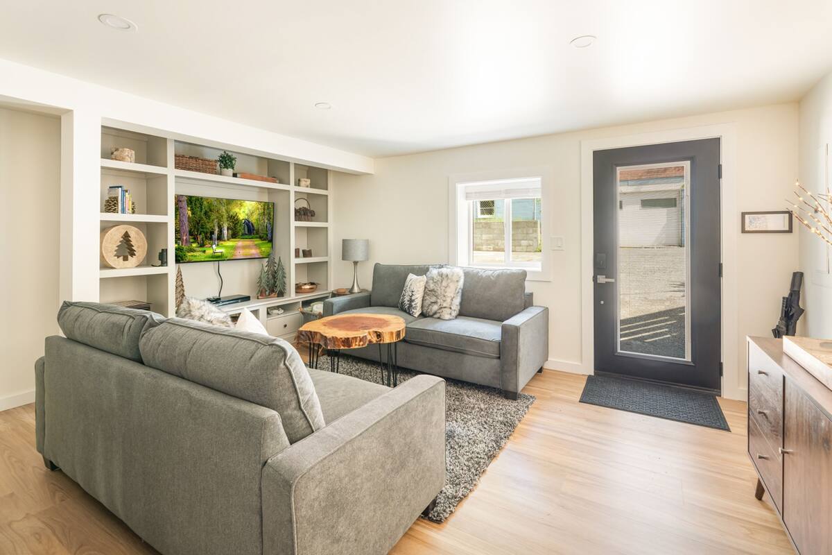 A modern living room with a grey sofa, a coffee table, and a TV on a white wall.
