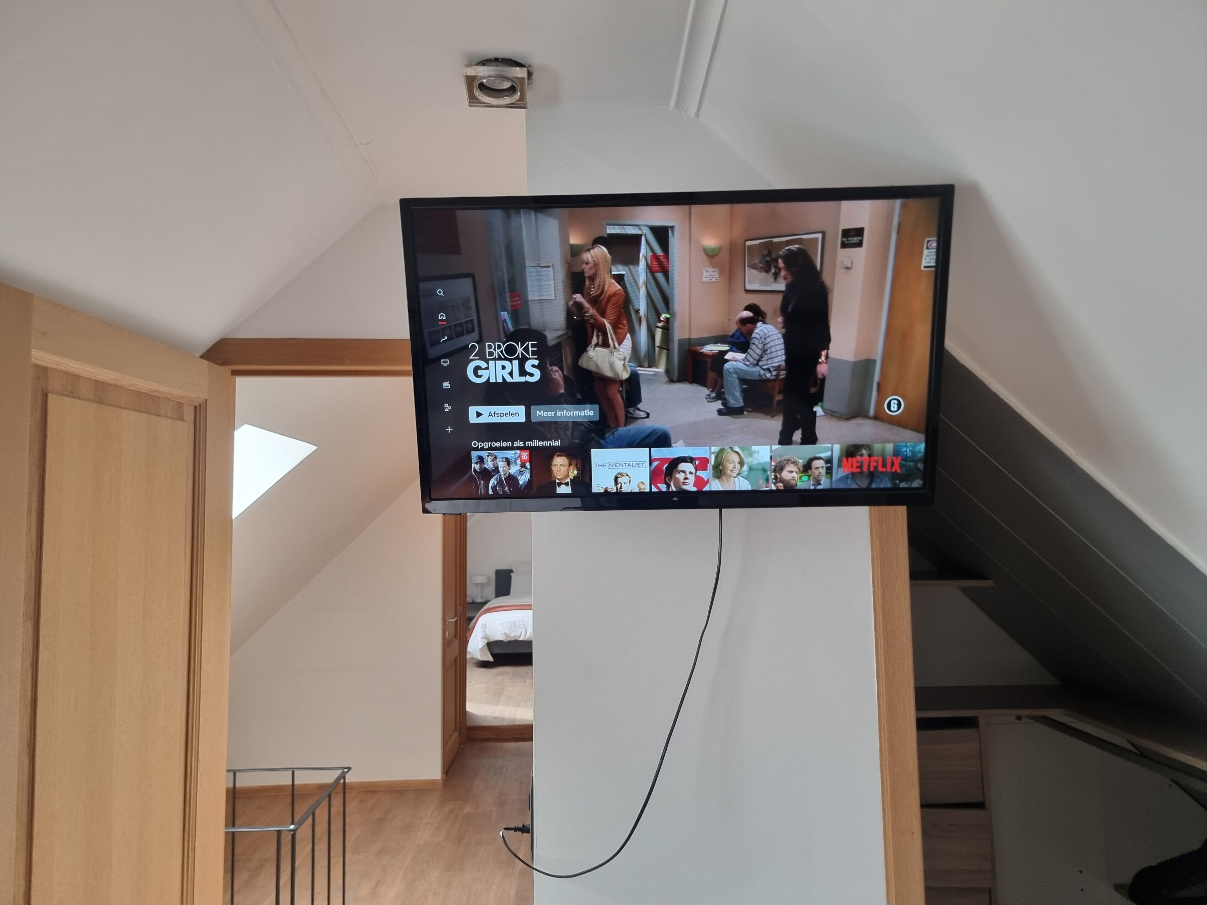 A television mounted on a wall displaying a show with a group of people in a room.