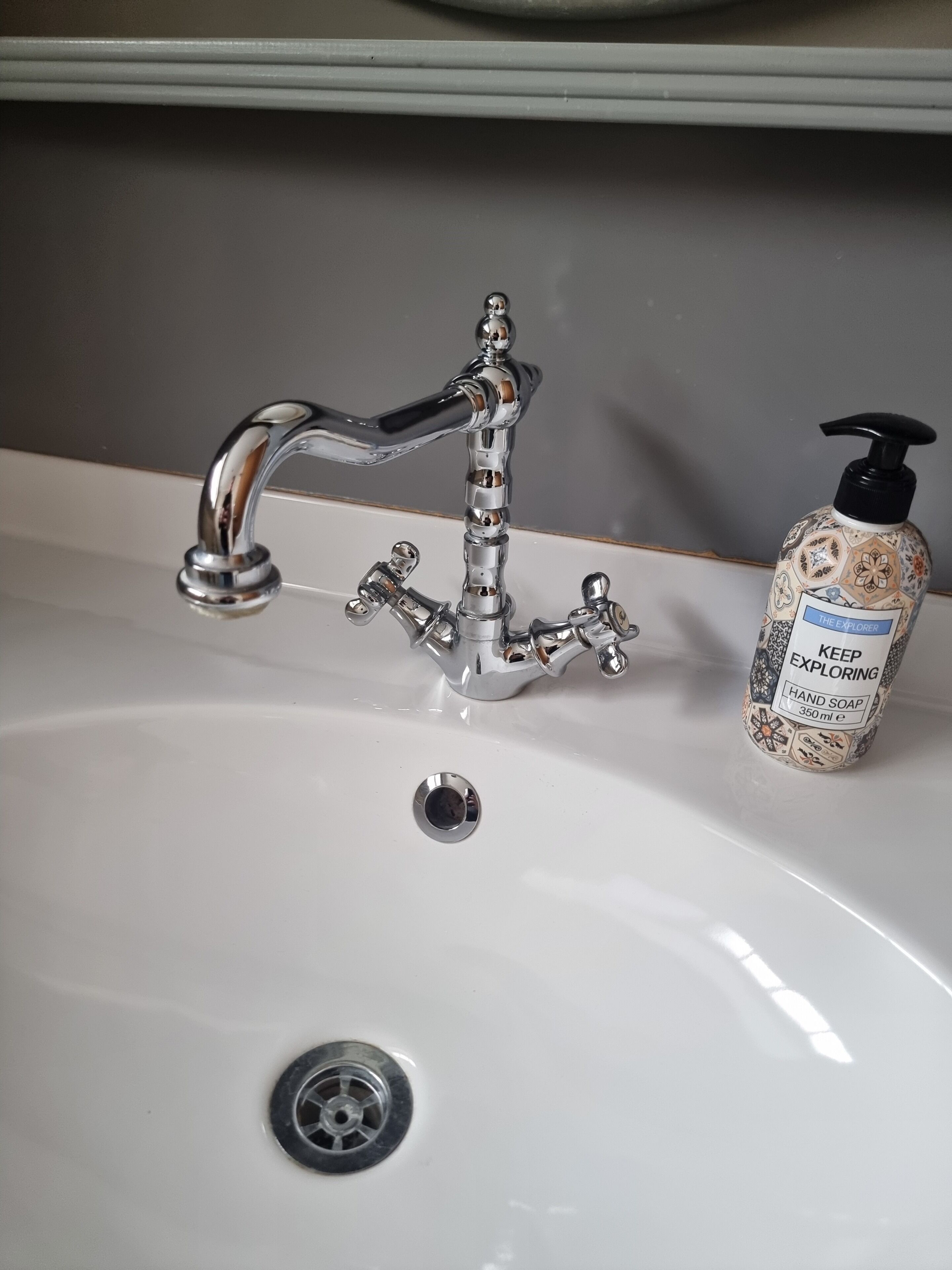Un lavabo de salle de bain avec un robinet chromé, un distributeur de savon et un drain.