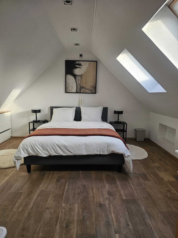 A bedroom with a sloped ceiling, a bed, bedside tables, and a skylight.