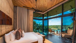 Ein modernes Schlafzimmer mit einem großen Bett, einem Deckenventilator und Blick ins Freie.