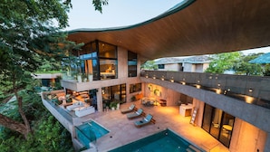 Ein modernes, mehrgeschossiges Haus mit Pool, Sitzgelegenheit im Freien und großen Fenstern.