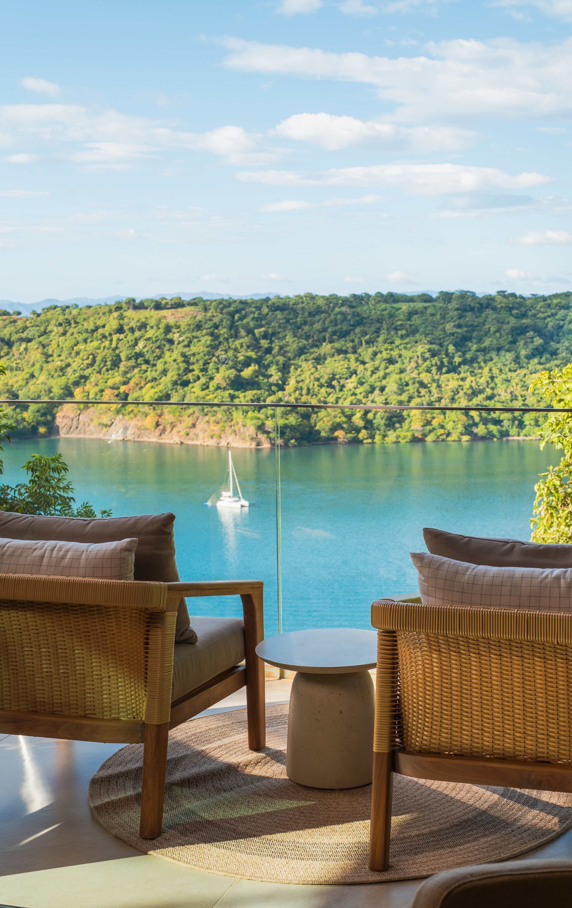 Vista de um lago com um veleiro, cercado por vegetação exuberante e colinas.