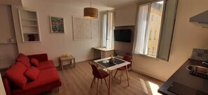 A compact living space with a red sofa, a dining table with chairs, a TV, and a window with curtains. - Studio de la Comédie, 2nd floor (Narbonne)