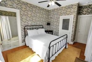Ein Schlafzimmer mit Bett, Deckenventilator, Nachttisch, einer Tür und einer Duschgelegenheit.