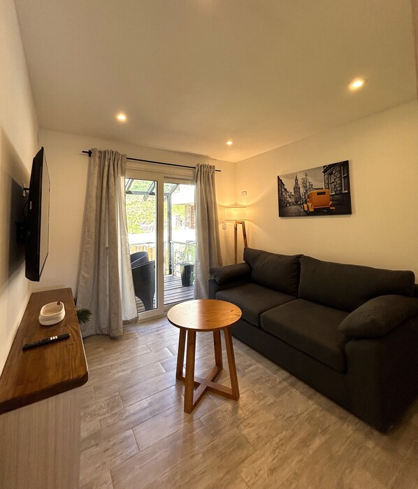 Un salon avec un canapé, une table en bois, un téléviseur fixé au mur et un tableau.