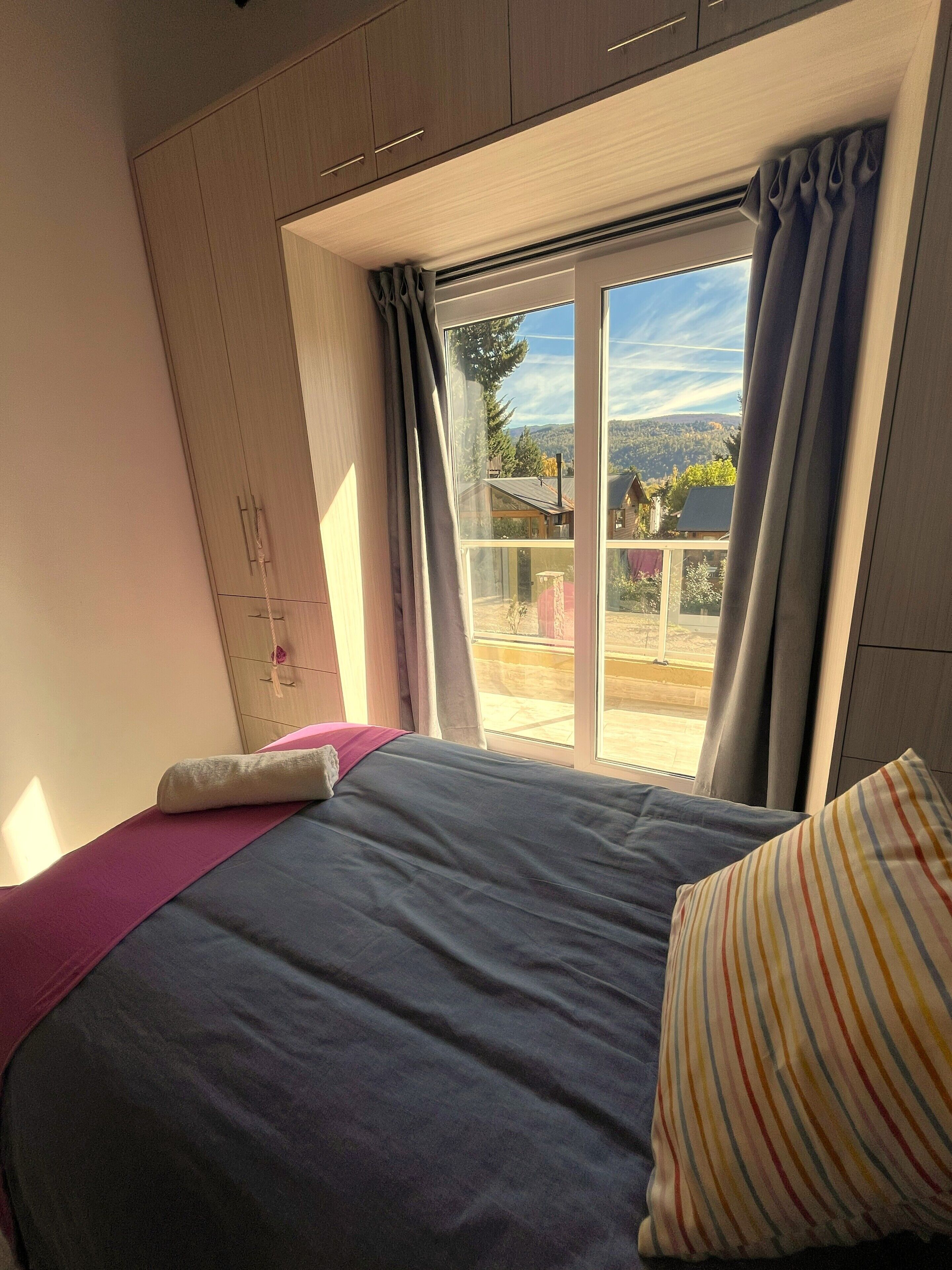 Un dormitorio con cama, ventana con cortinas y vista al exterior.
