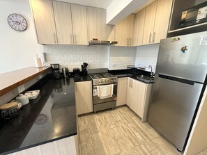 A modern kitchen with light wood cabinets, a stainless steel refrigerator, a gas stove, and a white tiled backsplash.
