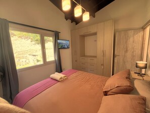 Ein Schlafzimmer mit Bett, einem an der Wand montierten Fernseher und einem Fenster mit Vorhängen.