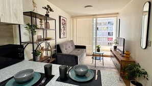 Een moderne woonkamer met een bank, een eettafel gedekt voor twee personen, een boekenkast en een stadsgezicht door een groot raam.