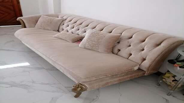 Un sofá beige con tapicería capitonada y cojines decorativos, sobre un piso de mármol.