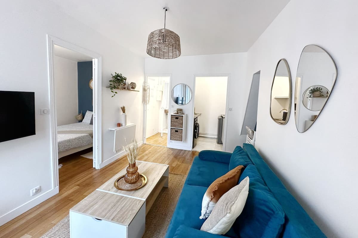 A modern living room with a blue sofa, a coffee table, and a TV. There is a doorway leading to another room.