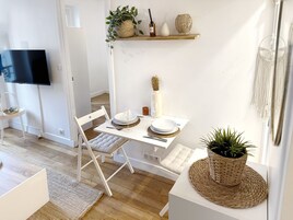 Un comedor moderno con una mesa blanca preparada para dos personas, un televisor montado en la pared y una estantería con objetos decorativos.