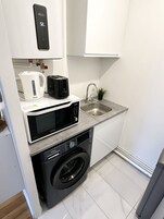 Una cocina compacta con microondas integrado, tostadora, hervidor y lavadora.