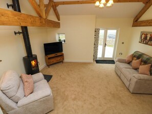 A living room with a fireplace, a sofa, a television, and a door leading outside. - Dairy Cottage (Swansea)