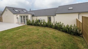 Ein zweistöckiges Haus mit geneigtem Dach, einer Veranda und einem kleinen Vorgarten mit Gras und Sträuchern.