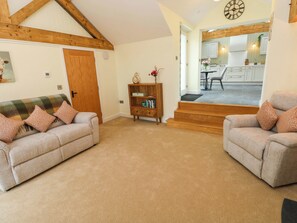 A living room with a sofa, a wooden bookshelf, and a staircase leading to a kitchen. - Dairy Cottage (Swansea)