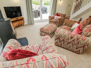 A living room with a sofa set, a television, and a sliding glass door leading to an outdoor area. - Barley Cottage (Swansea)